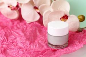 Green light cream in crystal jar with orchid flower on pink paper photo