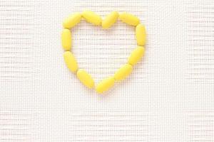 Vitamins pills on shape of heart, yellow tablets on table photo