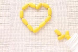 Vitamins pills on shape of heart, yellow tablets on table photo