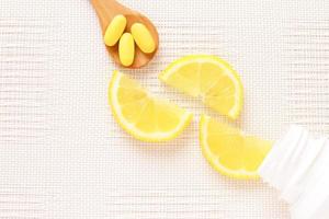 vitaminas amarillas en cuchara y rodajas de limón como fondo foto