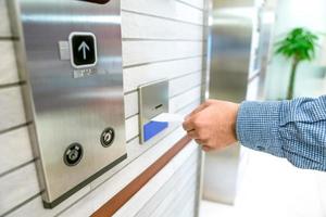 securing lift or elevator access control, man's hand is holding a key card lay up to insert in card hold for unlocking elevator doors before up or down. photo