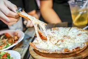 Woman's hand take pizza pices out from pizza plate in foodtruck event, Cheese's pizza is stretced by her. photo