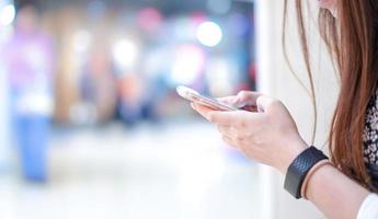 Young girl is holding smart phone in her hand beside angle view playing, typing, chatting, emailing with blurry bokeh department store behind. photo