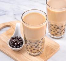 bebida popular de taiwán - té de leche de burbujas con bola de perla de tapioca en vaso de bebida sobre fondo de bandeja de madera de mesa blanca de mármol, primer plano, espacio de copia foto