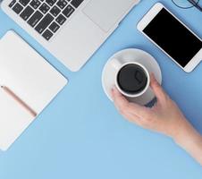 Business concept. Clean bright light blue office table desk, minimal style with laptop coffee and smart phone, copy space, top view, flat lay, mockup photo