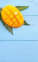 Fresh chopped mango with green leaves on bright blue color timber background. Above Top view, flat lay, copy space, close up. Tropical fruit concept. photo