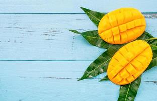 Fresh chopped mango with green leaves on bright blue color timber background. Above Top view, flat lay, copy space, close up. Tropical fruit concept. photo