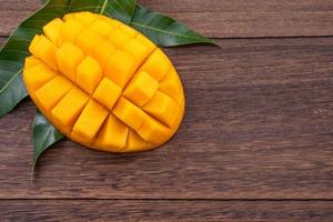 Fresh mango - beautiful chopped fruit with green leaves on dark wood background. Tropical fruit design concept. Flat lay. Top view. Copy space. photo