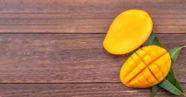 Fresh mango - beautiful chopped fruit with green leaves on dark wood background. Tropical fruit design concept. Flat lay. Top view. Copy space. photo