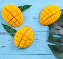 Fresh mango - beautiful chopped fruit with green leaves on bright blue timber background. Tropical fruit design concept. Flat lay. Top view. Copy space photo