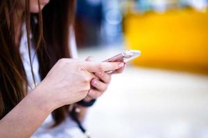 Young girl is holding smart phone in her hand beside angle view playing, typing, chatting, emailing with blurry bokeh department store behind. photo