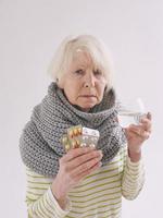 senior ill woman with glass of water and peels in scarf freezing on white background. Health care, crisis, oldness concept photo