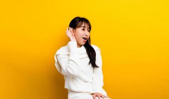 Eavesdropping girl Curious girl in white t-shirt poses alone on orange-yellow wall background studio portrait. concept of people's lifestyle copy space mockup Try to hear you with your hands close photo