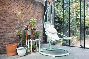 Interior design. Hanging wicker chair in the terrace with hanging decorative pots plants, brick wall background expose, go green environment, modern living. Bandung, INDONESIA-MARCH 17, 2022 photo