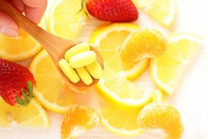 Vitamins pills on wooden spoon with lemon, orange, raspberry on background photo