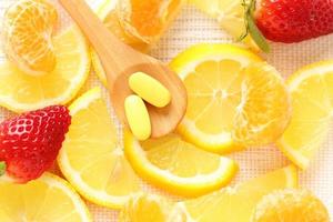 Vitamins pills on wooden spoon with lemon, orange, raspberry on background photo