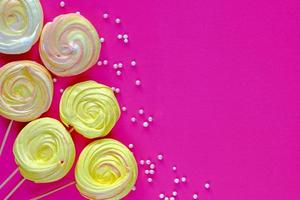 Flat lay with decorative meringues on sticks on pink background photo