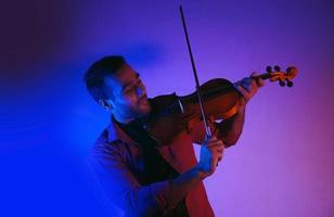 hombre tocando el violín en el estudio luces de neón con poca luz foto