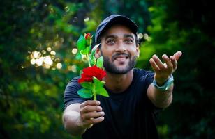 proponiéndole a su novia un hombre con una hermosa rosa roja que le da a la niña y le da la mano foto