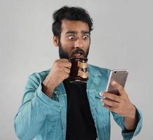 un hombre con una taza de café y un móvil viendo noticias y sorprendido por las malas noticias foto