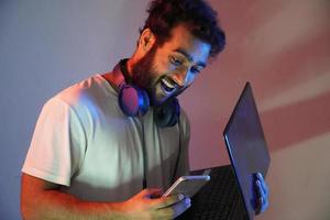 a man in studio with blue and red light having laptop and mobile photo