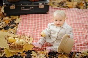 Little cute girl sits on a plaid, eats an apple and holds out a hat. Autumn photo shoot