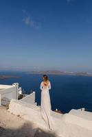 Beautiful bride In a white dress posing against the background of the Mediterranean Sea in Thira, Santorini.