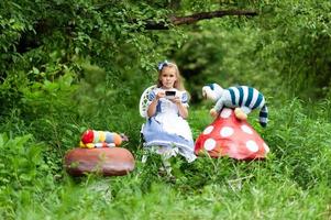 una niña linda con el disfraz de alicia del país de las maravillas organiza una fiesta de té en su mesa mágica. fotografiado en la naturaleza. foto