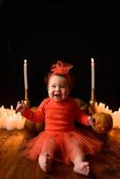 Little girl sits on a background of Jack pumpkins and candles on a black background. photo
