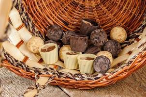 bombones y chocolate en una cesta sobre una mesa de madera foto
