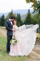 The bride and groom are hugging under an old oak tree. Wedding photo shoot in the mountains.