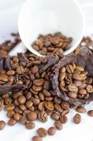 white cup with coffee beans and pieces of dark chocolate on a white tablecloth