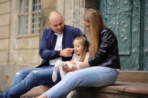 Parents and their daughter are sitting on the steps of an old church. photo