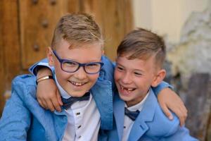 dos niños pequeños, los hermanos están vestidos con traje. los niños están parados en el parque y abrazándose. foto