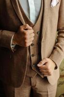 un hombre con un traje marrón de tres piezas. las manos se aferran a los lados de la chaqueta. de cerca