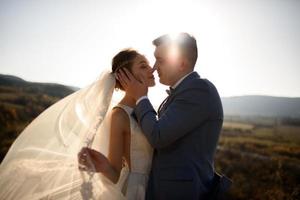 retrato de una joven novia hermosa y su marido en las montañas con un velo. el viento desarrolla un velo. fotografía de boda en la montaña. foto