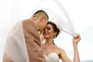 The bride and groom hug under a veil and gently bowed their heads to each other. photo