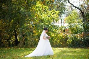 Portrait of a lonely bride on a background of an autumn park. The girl took refuge under a veil with which the wind develops. photo