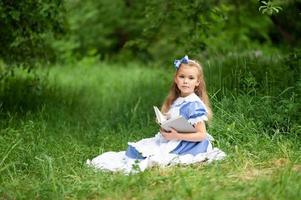una niña linda disfrazada de alicia del país de las maravillas está leyendo un libro. foto