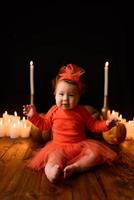 Little girl sits on a background of Jack pumpkins and candles on a black background. photo