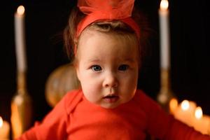 Little girl sits on a background of Jack pumpkins and candles on a black background. photo