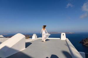 Beautiful bride In a white dress posing on the roof of the house against the background of the Mediterranean Sea in Thira, Santorini.