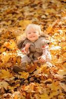 una niña linda está sentada en un montón de hojas. Otoño.