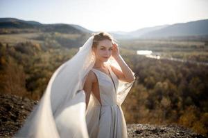 Portrait of a young beautiful bride in the mountains with a veil. The wind develops a veil. Wedding photography in the mountains. photo