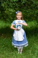 una niña linda con un disfraz de alicia sostiene un viejo reloj antiguo. foto