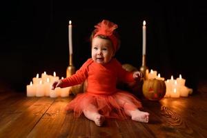 Little girl sits on a background of Jack pumpkins and candles on a black background. photo