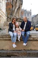Parents and their daughter are sitting on the steps of an old church. photo