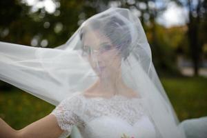 retrato de una novia solitaria sobre un fondo de un parque de otoño. la niña se refugió bajo un velo con el que se desarrolla el viento. foto