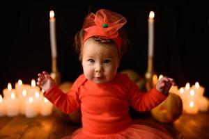 Little girl sits on a background of Jack pumpkins and candles on a black background. photo