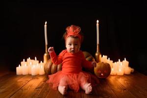 Little girl sits on a background of Jack pumpkins and candles on a black background. photo